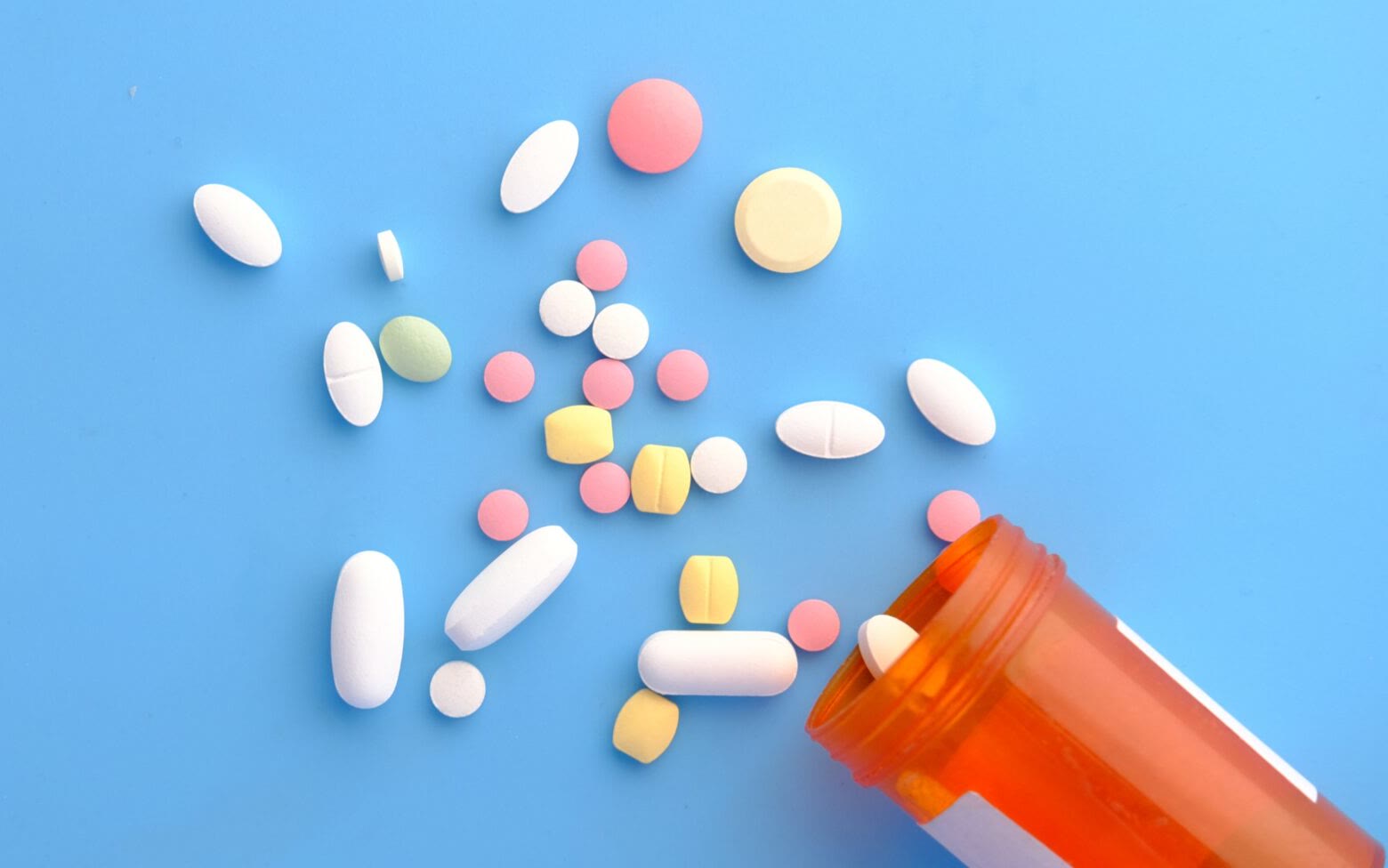 Assorted tablets and capsules beside a prescription bottle